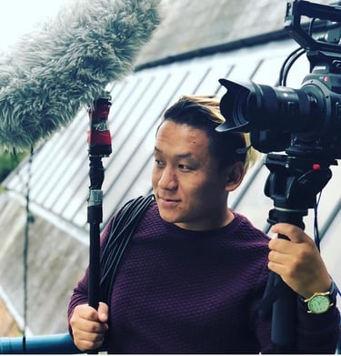 a man in a purple sweater holding a microphone and a video camera
