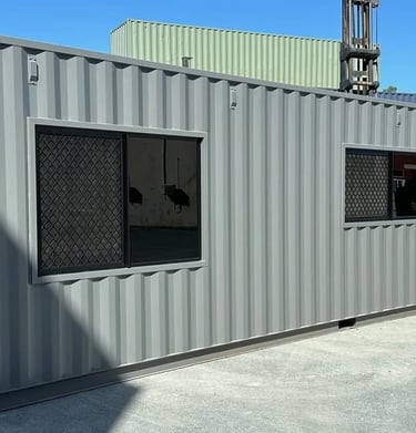Modified grey shipping container office with installed glass windows and security screens.