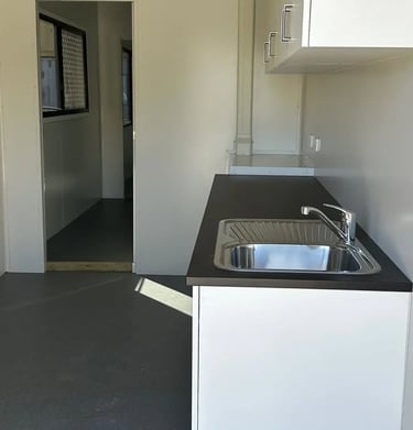 Interior of a modern portable site office cabin featuring a kitchenette with a stainless steel sink and dark countertop.