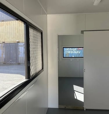 Interior of a portable site office container with a sliding door and window overlooking a shipping yard.