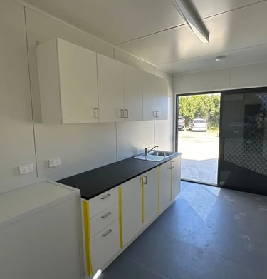 Modern portable container kitchen featuring white cabinetry, black countertop, and stainless steel sink.