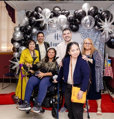 Diverse group of smiling people with disabilities posing at an anniversary party with silver and black balloons.