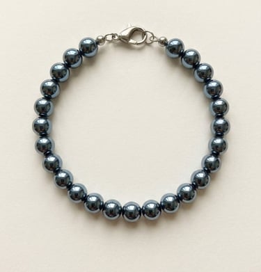 Polished dark grey hematite bead bracelet with a silver lobster claw clasp on a cream background.