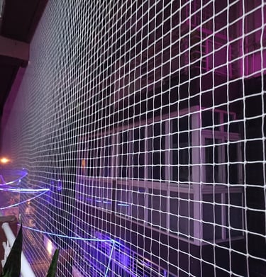 Wide shot of a high-rise apartment balcony fully enclosed with a transparent safety net, with childr