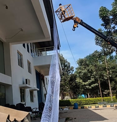 Team of Arjilli Safety Nets professionals working together to secure pigeon nets on a warehouse exte