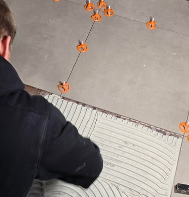 Professional contractor installing large format floor tiles with orange leveling spacers and thinset mortar.
