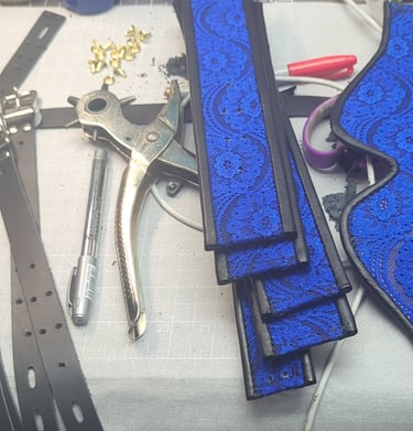 Handmade blue lace lace and leather pieces and eye mask on a workbench with leather crafting tools.