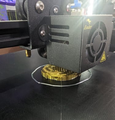 An Ender 3D printer extruding golden silk PLA filament to create a detailed circular model on a black print bed.