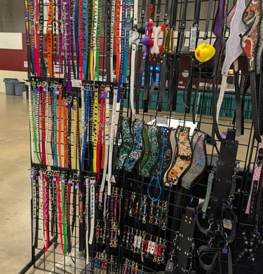 A retail display rack featuring a variety of colorful pet collars, harnesses, and leather accessories.
