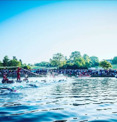 Triathletes swimming in a lake at the start of Challenge Roth with spectators on the shore.