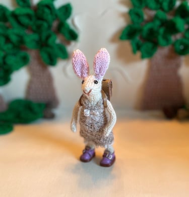a small knitted bunny ornament wearing a crochet dress and handmade leather shoes and satchel
