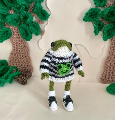 a dot pebbles knitted frog in a jumper with a crochet frog motif