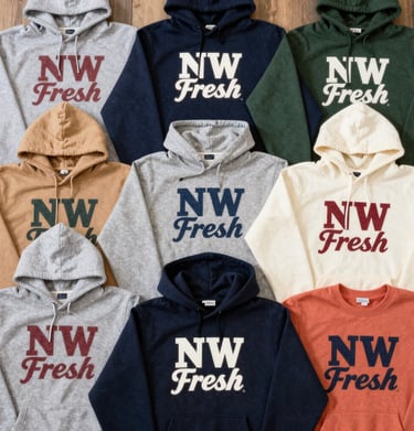 A flat lay of hoodies in earthy tones spread over a wooden table with pinecones and fallen leaves.