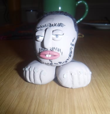 Handmade clay sculpture of a bearded man's head sitting on two large feet on a wooden table.