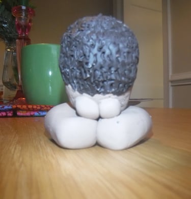 Handcrafted clay sculpture of a person kneeling in prayer or meditation on a wooden table.