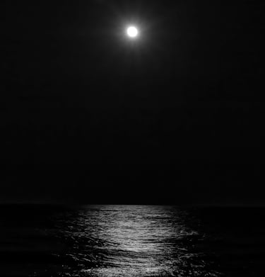 A black-and-white photograph of the full moon rising above the ocean and its moonlight on the water in Cape May, NJ.