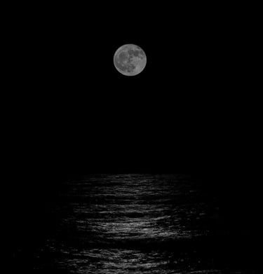 A black-and-white photograph of the full moon rising above the ocean and its moonlight on the water in Cape May, NJ.