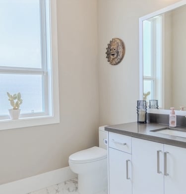 Modern bathroom interior featuring white vanity cabinets, grey countertop, and a sun-shaped wall decor.