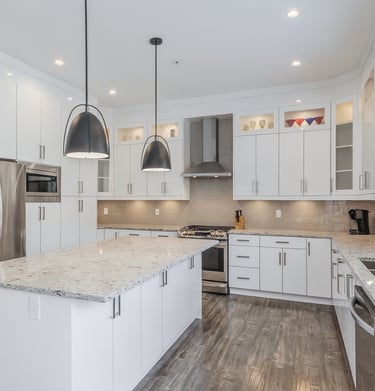 Modern white kitchen with granite countertops, stainless steel appliances, and black pendant lights.