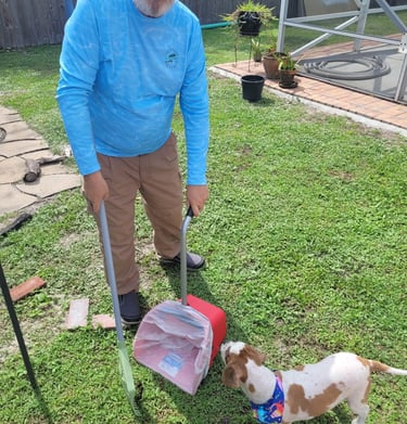 Robert using a sanitized scooper to remove waste from a customers back yard, small dog watching him