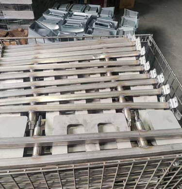 Stacked industrial stainless steel handrail components in a wire storage crate for manufacturing.