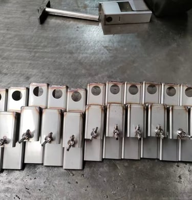 Custom fabricated stainless steel metal brackets with wing nuts on a factory workbench.
