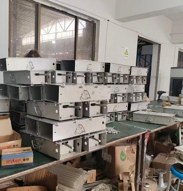 Worker assembling stainless steel sheet metal enclosures in a factory production line.