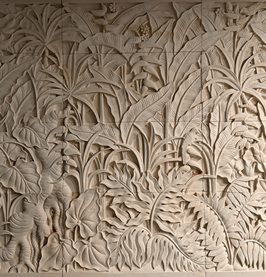 Hand-carved limestone wall relief featuring a lush tropical jungle scene with palm leaves and exotic birds.