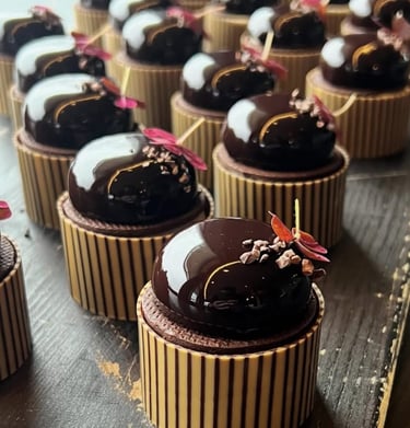 Gourmet dark chocolate mousse domes with mirror glaze and gold leaf garnish on striped pastry cups.