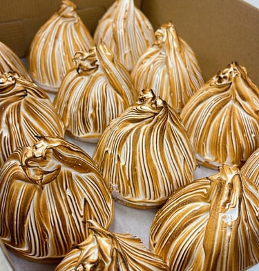 Gourmet toasted meringue tarts with golden brown peaks arranged in a bakery pastry box.