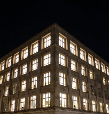 Night view of a illuminated architectural facade, carbon black sky, warm light spilling from windows, sharp geometric forms.