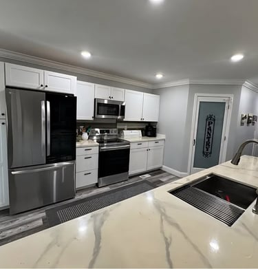 Modern kitchen with white cabinets, stainless steel appliances, and a marble island with a sink.