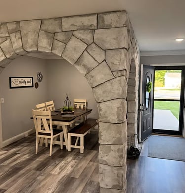 Rustic dining room with a stone archway, dark wood table, and grey laminate flooring.