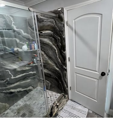 Modern walk-in shower with black and white marbled stone panels and glass doors.
