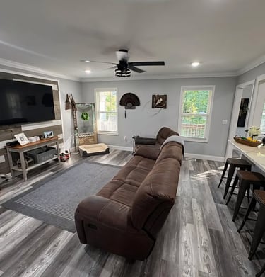 Modern living room with brown reclining sofa, wood accent wall, and grey vinyl plank flooring.