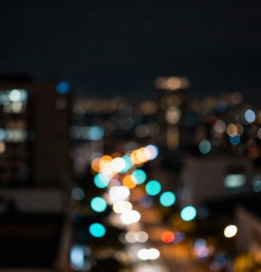 Artistic bokeh shot of city lights in Bogotá, showcasing deep blacks and vibrant neon cyan circles. Cinematic and urban.
