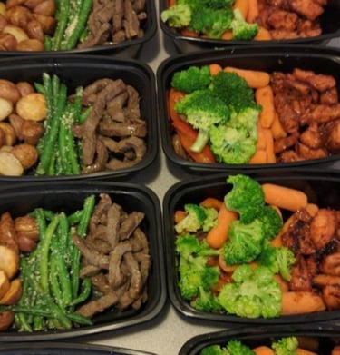 Meal prepped food in black Tupperware including steak, carrots, broccoli, asparagus and potatoes