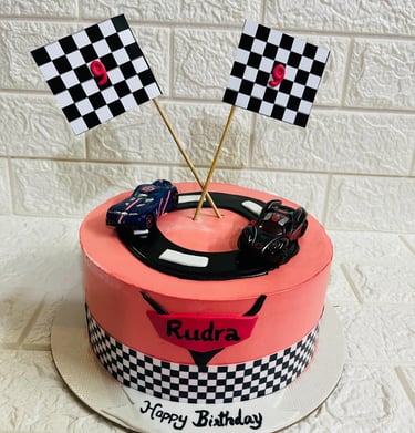 Customized race car themed birthday cake with checkered flags and toy cars for a 9th birthday party.