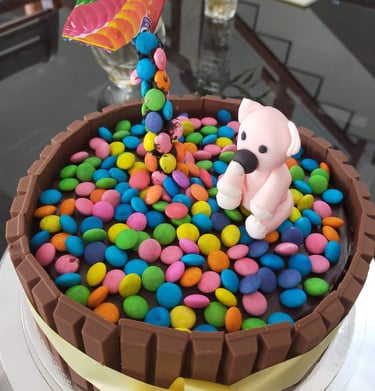 Chocolate Kit Kat cake decorated with colorful chocolate candies and a pink fondant bear topper.
