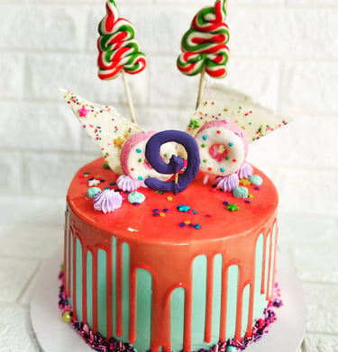 Colorful 9th birthday drip cake with pink glaze, lollipops, donuts, and sprinkles.