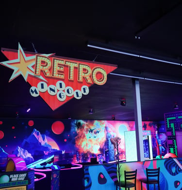 A glowing neon retro mini golf sign hanging over a blacklight indoor putt-putt course.