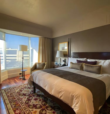 Habitación de hotel con gran ventanal, cama doble y pared marrón