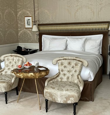 Habitación de hotel de lujo con cama en el medio y 2 sillones y una mesa delante.