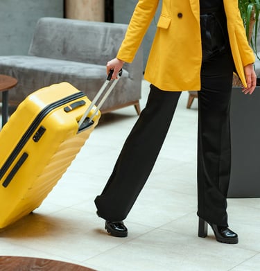 A person in a yellow blazer pulling a matching yellow hardshell suitcase through a modern hotel lobby.