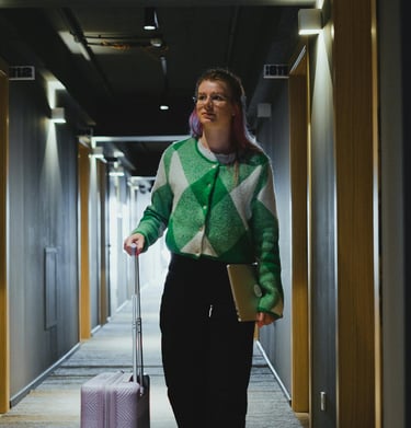 Una chica con un ordenador portátil y una maleta en el pasillo del hotel.