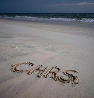 Cinematic vertical shot of the empty beach at twilight, the remnants of sand art visible, soft sand off-white meeting the dark sea.