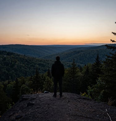 A silhouette of a person standing on a ridge looking out over a vast forest valley at dusk, North American wilderness, contemplative and serene mood.