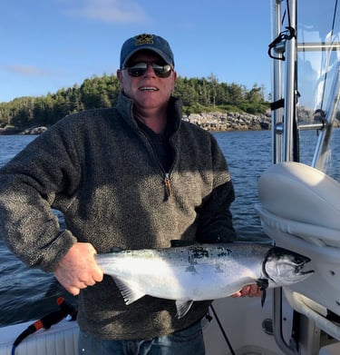 A man on a fishing boat holds a large silver salmon caught during a deep-sea fishing trip.