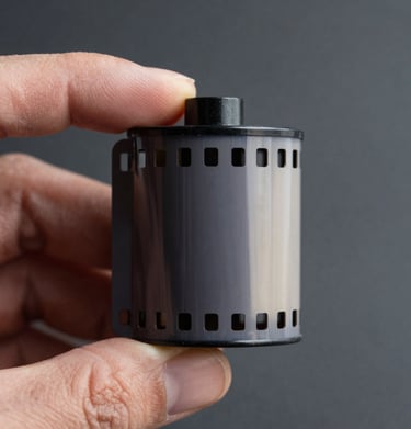 Macro shot of a vintage 35mm film strip held by a hand in an Angolana studio, moody lighting, featuring dark slate grey and off-white textures.