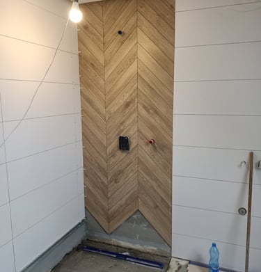 Modern bathroom shower renovation featuring vertical oak herringbone tiles and white wall panels.